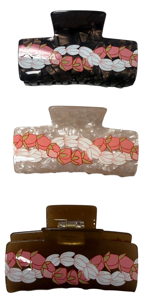Three hair claw clips with a repeating pink and white floral pattern, shown in black, clear, and brown translucent plastic on a light gray surface.