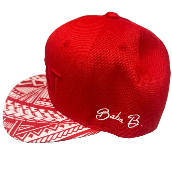 A red baseball cap with a red and white patterned brim and white cursive 'Baba B.' embroidery on the side, resting on a gray surface.