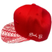 A red baseball cap with a red and white patterned brim and white cursive 'Baba B.' embroidery on the side, resting on a gray surface.