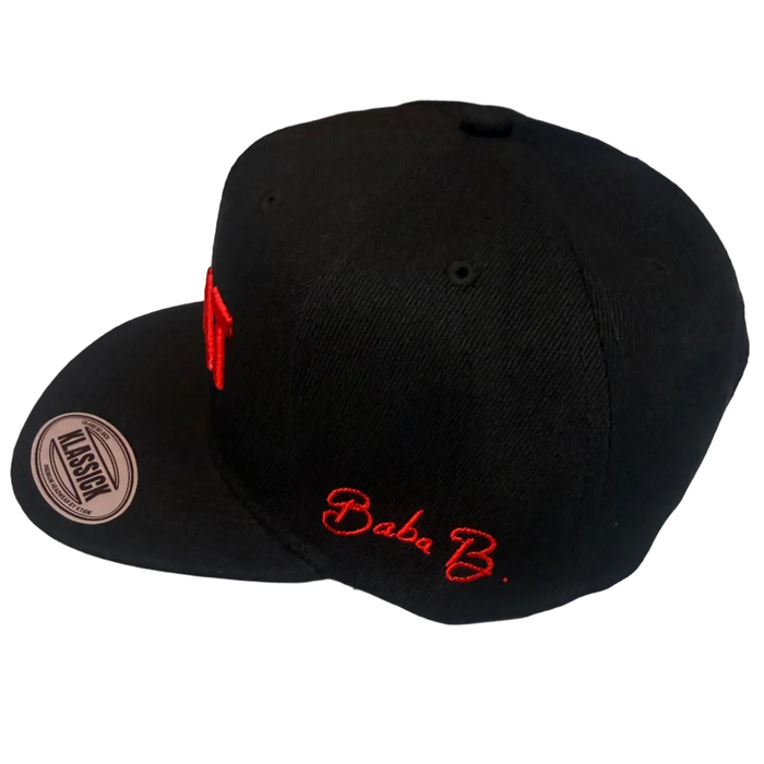 A black snapback cap with red embroidered 'Baba B.' text on the front and a visible Allstar sticker on the brim, photographed on a light tabletop.
