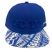 A royal blue snapback cap with 'DEDEDO' embroidered on the front and a blue and white geometric patterned visor, displayed on a light gray surface.