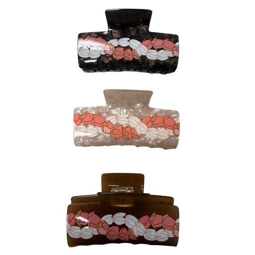 Three hair claw clips with a repeating pink and white floral pattern, shown in black, clear, and brown translucent plastic on a light gray surface.