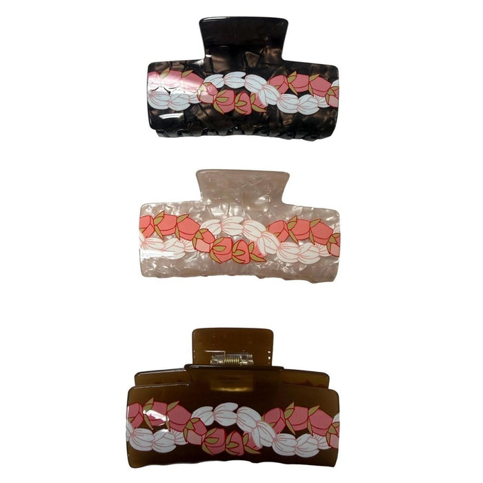 Three hair claw clips with a repeating pink and white floral pattern, shown in black, clear, and brown translucent plastic on a light gray surface.