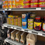 Shelving unit with various food products including canned goods and bottles in a store setting.